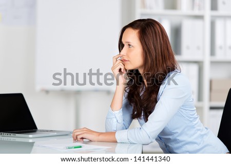 Worried businesswoman sitting at her desk staring into the distance thinking