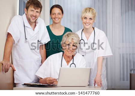 Portrait of smiling male and female doctors with laptop at desk in hospital