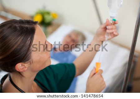 Nurse adjusting infusion bottle with patient lying on bed in hospital