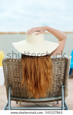 Rear view of a redhead woman in straw hat sitting on deck chair at roof terrace