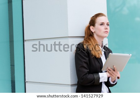 Smart young redhead businesswoman with tablet PC looking away