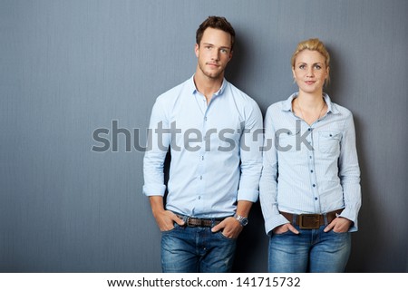 Portrait of a serious young man and woman looking in camera and standing against gray background