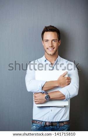 Portrait of a smiling young man standing with white ring binder against gray background