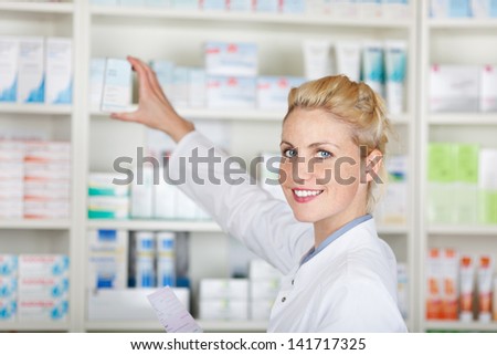 Portrait of a smiling female pharmacist with prescription in front of medicines at drugstore