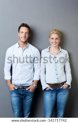 Portrait of a smart young man and woman smiling and standing against gray background