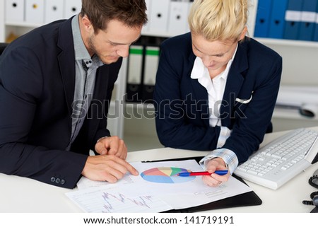 Portrait of a smart young businessman and woman looking at graphs sitting by computer at office desk