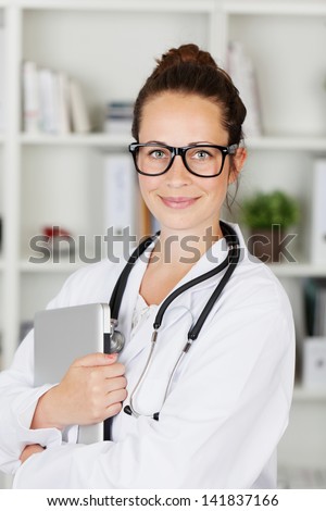 Attractive friendly young female doctor or medical student wearing glasses holding a laptop computer in her arms