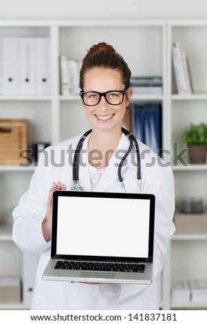 Attractive smiling young doctor or medical practitioner displaying her homepage on a handheld laptop computer which has blank white copyspace for your text