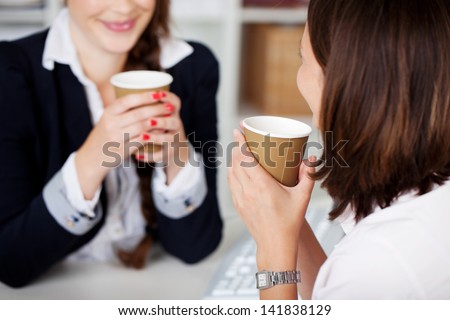 Office coffee break with two female colleagues sitting chatting over cups of coffee