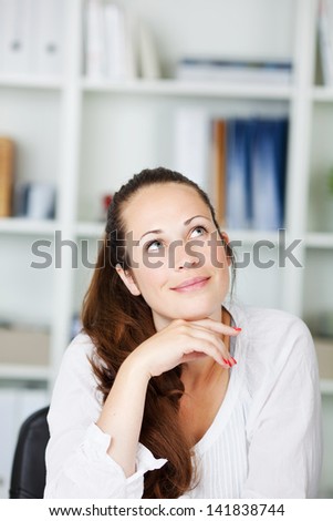 Thoughtful attractive young woman sitting with her chin resting on her hand looking up into the air