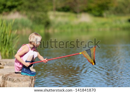 Little girl waiting for fish in at lake squatting down on the rocks holding her fishing net at the ready