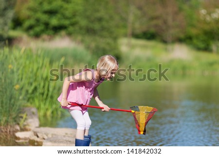 Young girl catching fish at the lake standing in her gumboots on the rocks poised with her net at the ready