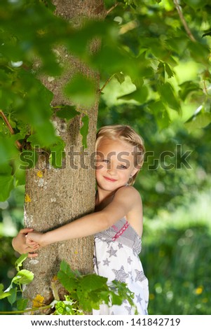 Beautiful young girl hugging a tree to show her appreciation of nature standing with her arms around the trunk under the green leaves