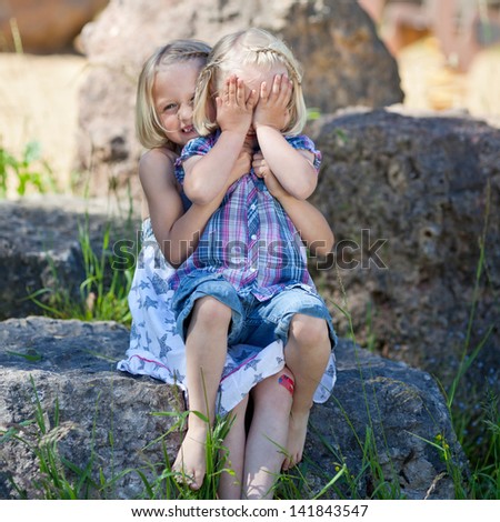 Shy little girl covering her face while sitting on the lap of her young sister posing for their portrait outdoors