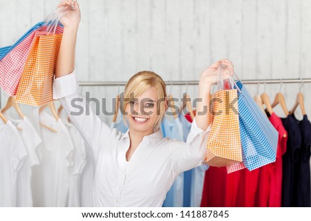 Happy young woman with arms raised carrying shopping bags in shop
