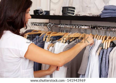 Mid adult woman choosing shirt from rack in clothing store