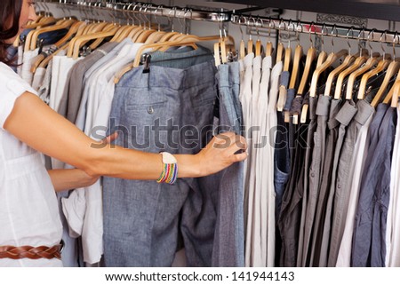Mid adult woman choosing trouser from rack in clothing store