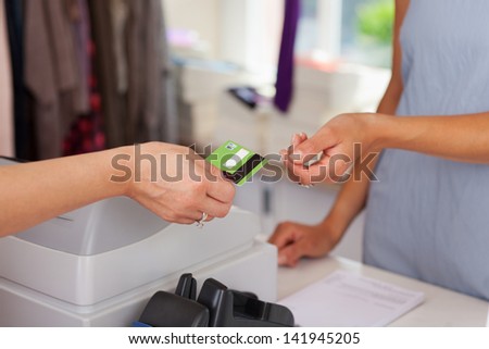 Closeup of saleswoman giving credit card to female customer at boutique counter