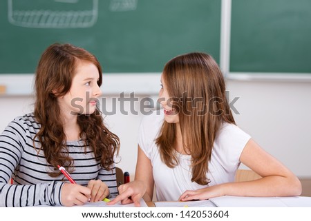 Two cheerful students talking while writing notes in school room