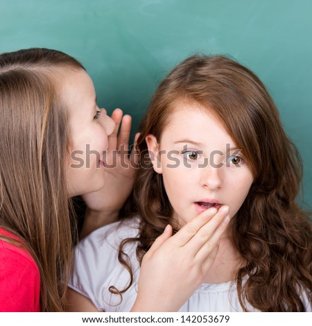 Two children sharing a secret in front of blackboard