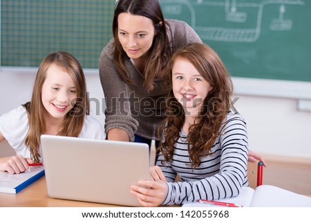 Teacher teaching her two students with laptop inside the classroom