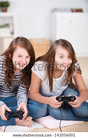 Two young girls happily playing video games in a console sitting on the living-room floor
