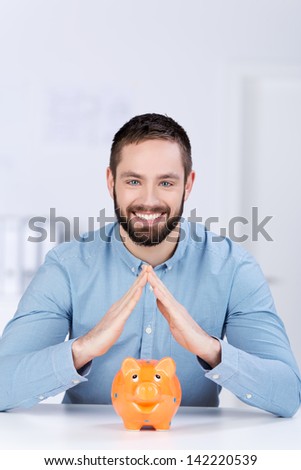 Portrait of happy young businessman joining fingers over piggybank representing home investment in office