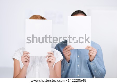 Businessman and businesswoman holding blank paper in front of their faces in office