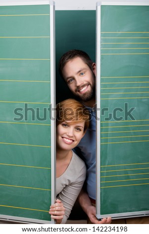 Portrait of happy male and female students hiding behind green panels
