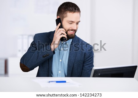 Young businessman working on computer while using mobile phone at desk in office
