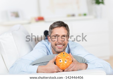 Portrait of mature man holding piggybank while lying on sofa at home