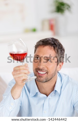 Portrait of happy mature man looking at wineglass at home