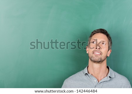 Thoughtful mature male teacher against blank blackboard - copy space for text