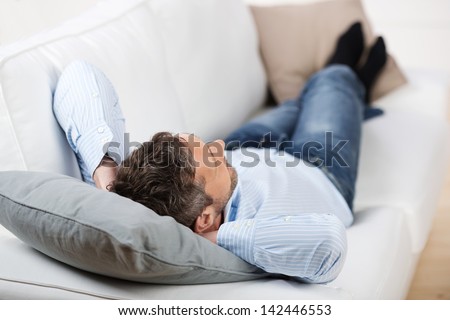 Rear view on mature man with hands behind head lying on sofa at home