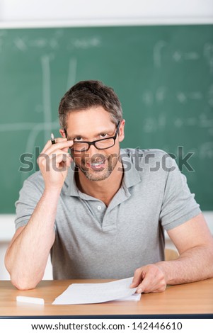 Portrait of male teacher checking examination papers at bench in classroom