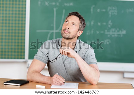 Thinking male teacher at bench in classroom