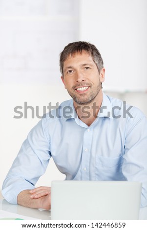 Portrait of happy mature businessman with laptop at office desk