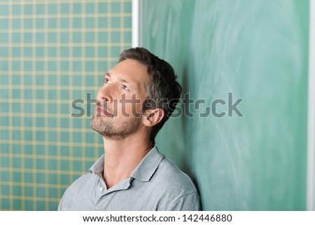 Thoughtful handsome mature male teacher against blank blackboard