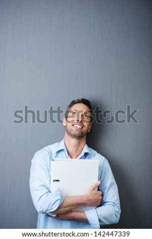 Thoughtful mature businessman holding binder while looking up against blue wall