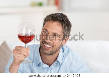 Portrait of smiling mature man looking at wineglass at home