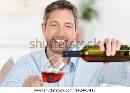 Happy mature man pouring wine in wineglass at home