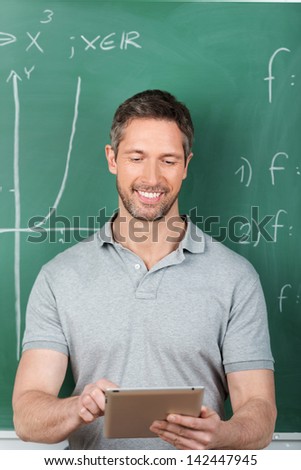 Happy male teacher using digital tablet against chalkboard in classroom