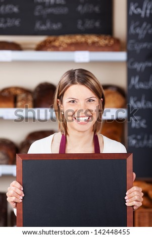 Smiling friendly bakery worker holding a blank chalkboard or slate with copyspace for your text