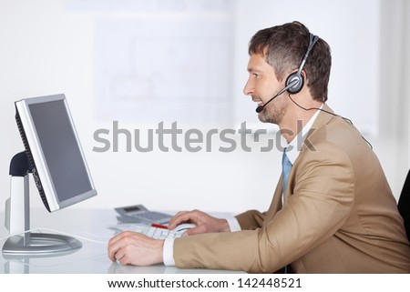 Smiling mature male businessman with headset looking at computer screen in office