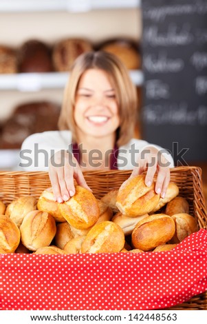 Friendly bakery worker selecting rolls for a customer from a large flat wicker basket