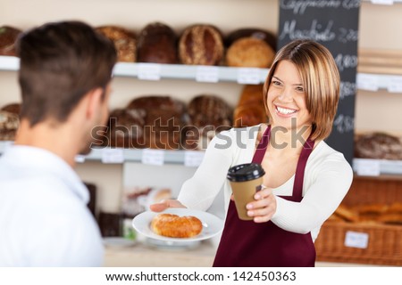 Female baker giving coffee and croissant to male customer in the bread store