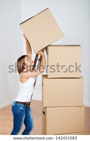 Pretty young woman stacking cardboard boxes packed with household goods when preparing to move home