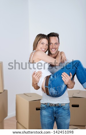 Loving man carrying his wife over the threshold of their new home into a room full of packed cartons