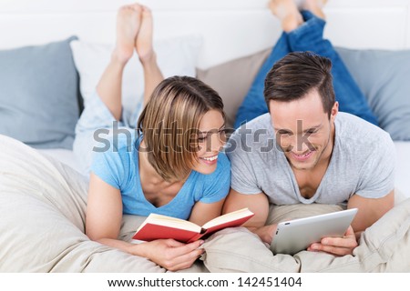 Smiling Young Couple In Bed With A Book And Tablet