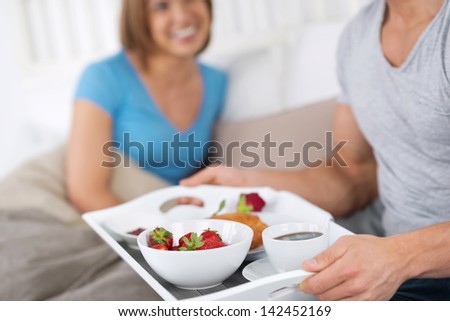 Hand s of a man carrying a tray laden with breakfast and a single red rose for his wife in bed